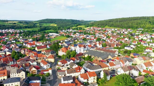 Malerische Luftaufnahme von Auerbach in der Oberpfalz mit der markanten Stadtpfarrkirche, traditionellen roten D&auml;chern und idyllisch gr&uuml;ner Landschaft im Hintergrund unter blauem Himmel.