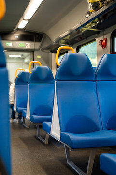 Row of blue seats with yellow handrails inside modern commuter train carriage