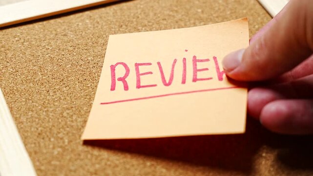 REVIEW in red capitals underlined on a peach note, set straight across a warm cork board with a wooden frame edge. Good for reviewing documents, code review, peer review, proofreading and quarterly r