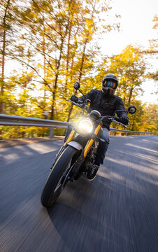 A motorcyclist overtakes a small yellow car on an asphalt road through the forest. The moving shot captures both vehicles in motion against a wooded roadside backdrop.