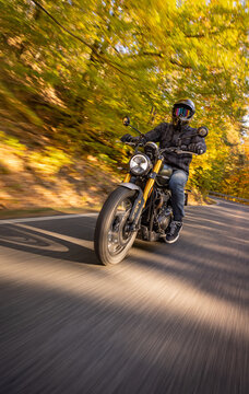 A motorcyclist overtakes a small yellow car on an asphalt road through the forest. The moving shot captures both vehicles in motion against a wooded roadside backdrop.