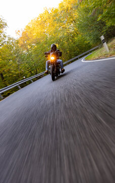 A motorcyclist overtakes a small yellow car on an asphalt road through the forest. The moving shot captures both vehicles in motion against a wooded roadside backdrop.
