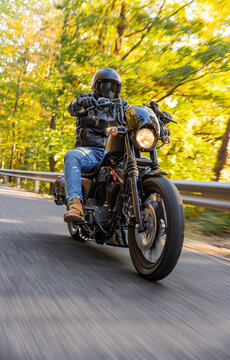A motorcyclist overtakes a small yellow car on an asphalt road through the forest. The moving shot captures both vehicles in motion against a wooded roadside backdrop.