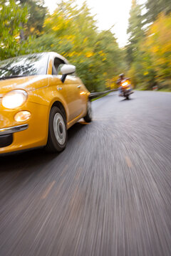 Motorcyclist Overtaking a Small Yellow Car on a Forest Road