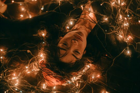 Woman lying upside down gently tangled in warm glowing string lights indoors