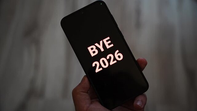 Bye 2026 message glowing in pink letters on a black smartphone screen held in one hand as the year comes to an end. Farewell to the old year for New Year Eve countdown, year in review and goodbye 202