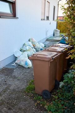 Brown organic waste bins on wheels and yellow plastic garbage bags stacked next to a house wall. Waste sorting and recycling management concept in Germany outdoor.