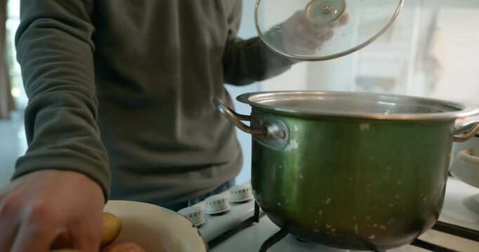 Close-up male hands put potatoes in pot with boiling water. 4K 10-bit