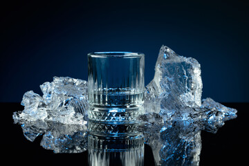 Crystal glass of vodka and ice shards against a black reflective background. © Igor Normann
