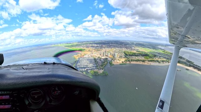 Cessna 172 cockpit view showing a small plane flying over Almere Haven, waterfront city and Markermeer lake in the Netherlands with spinning propeller on nice summer day