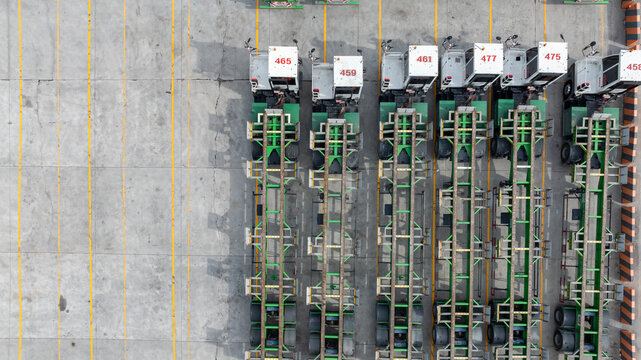 Aerial view port terminal trucks and chassis trailers lined up in logistic yard, Terminal tractors parked with bombcart trailers at container port terminal.