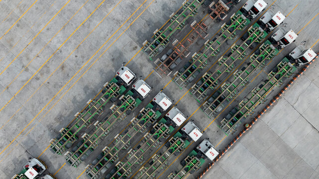 Aerial view port terminal trucks and chassis trailers lined up in logistic yard, Terminal tractors parked with bombcart trailers at container port terminal.