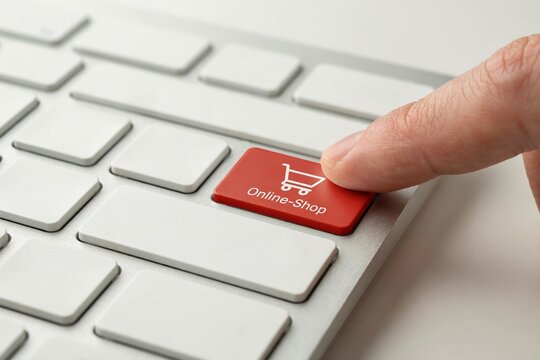 A finger pressing a red online shop button on a white computer keyboard in bright light.