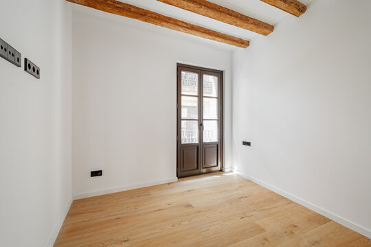 Empty room with wooden beams and a large window. Light-colored wooden floor. Minimalist design with white walls. Ideal for interior design concepts.