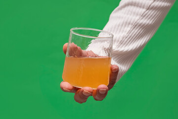 Hand holding a glass of orange juice against a green background. This beverage image is ideal for health, nutrition-focused, and creative video editing projects using chroma key. © ismailgazel