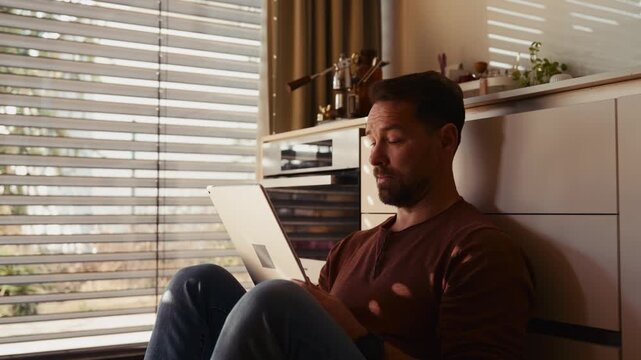 Side view of man using smart home app sitting on floor.