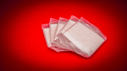 Stack of individually wrapped sanitary pads on a vibrant red background © İdil Toffolo