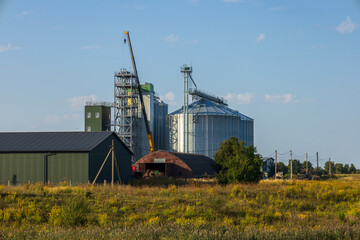 Rising majestically, the grain silos dominated the serene countryside, surrounded by fields and industrial structures, under a sunny sky © ProStockPhoto