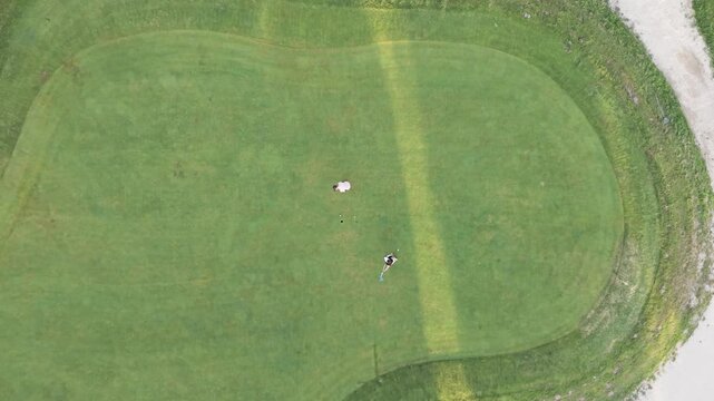Two professional golfers playing on a beautiful green. One player putts the ball towards the hole in a display of skill and precision