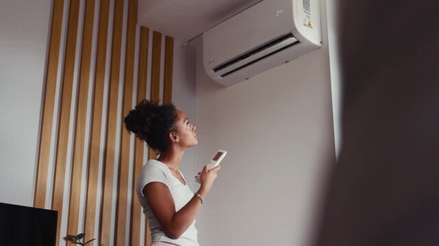 Young woman setting home temperature using air conditioner remote.