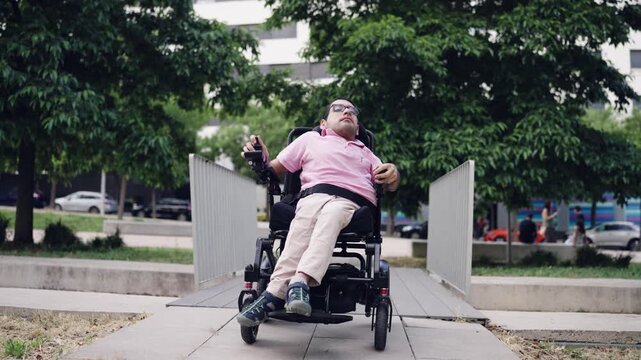 Man with a physical disability, spina bifida, using his motorized wheelchair to cross a ramp in a city park for accessibility