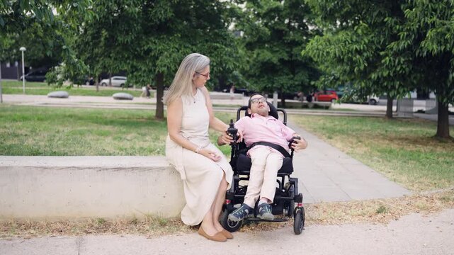 Caring mother spending quality time with her disabled adult son in a wheelchair. Loving family enjoying a quiet moment together outdoors