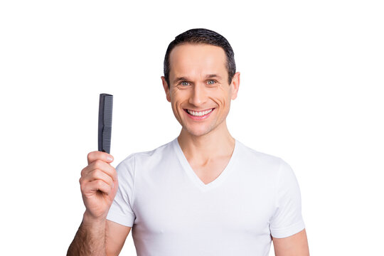 Portrait of trendy, stylish, experienced, brunet, neat man with beaming smile, having comb in hand, wearing white t-shirt, looking at camera, isolated on grey background