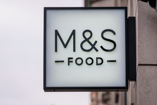 LONDON, UK. 15th  February 2025. Close-up of an illuminated square M&S Food logo sign hanging on a stone building wall.