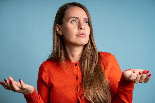 Young girl gesturing uncertainty or doubt on blue background. Casual portrait expressing bewilderment and ignorance about something.