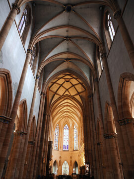 Stunning view of Saint-Martin Gothic church nave featuring ribbed vaulting, tall columns, and illuminated altar. Colmar, Alsace, France