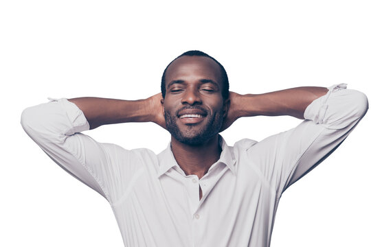 Portrait of cheerful, glad, positive, relaxed man with close eyes in white elegant shirt holding hands behind the head, dreaming about vacation, remember good memories, isolated on grey background
