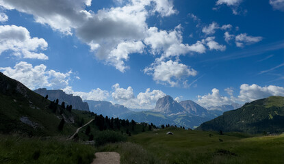 Fototapeta premium View of beautiful landscape in the Alps with fresh green meadows and mountain tops in the background on a sunny day with blue sky and clouds in summertime. Alpe di Cisles, Seceda Ridgeline, Dolomiti ,