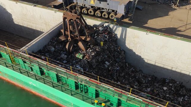 Industrial Crane Loading Scrap Metal Into a Large Green Cargo Ship