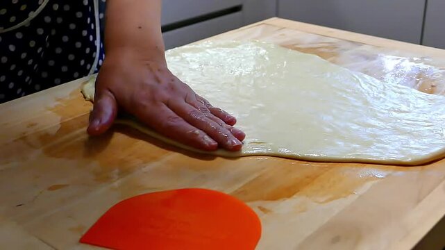 Chef cutting rolled dough with a kitchen knife on a wooden board