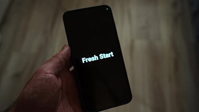 Fresh Start in glowing cyan letters on a smartphone held by a man in dim, warm light over a wooden floor. A motivational message for new beginnings, January resolutions, career change, second chances