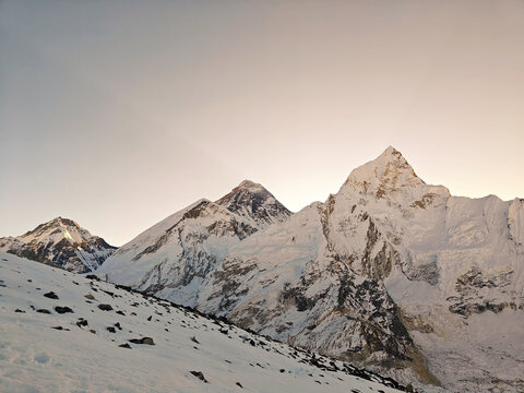 Snow-covered mountains rise sharply against a clear sky during early morning hours in a remote location