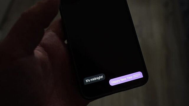 Chat bubbles pop up on a smartphone in a dark room, saying it is midnight, Happy New Year 2027 and a toast to new adventures. A conversation between friends at the New Year Eve countdown, full of tex