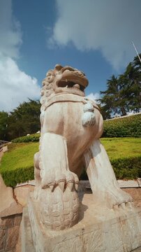 Slow-motion pan across a traditional Chinese guardian lion statue under bright blue sky.