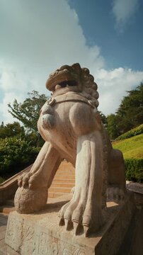 Slow-motion pan across a traditional Chinese guardian lion statue under bright blue sky.