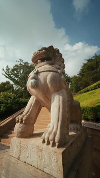 Slow-motion pan across a traditional Chinese guardian lion statue under bright blue sky.