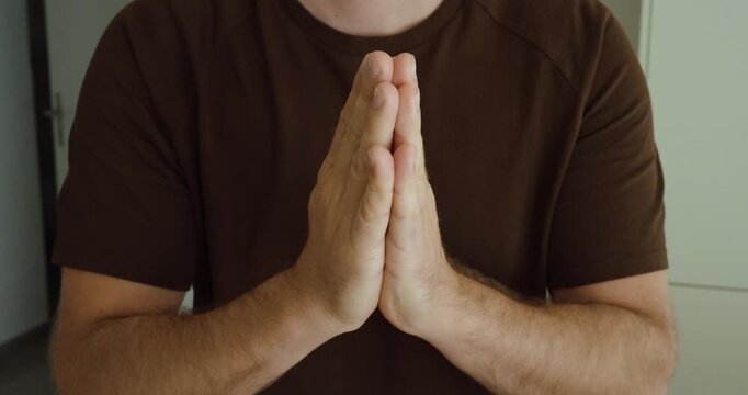 Close up of a man pressing his palms together in a pleading gesture