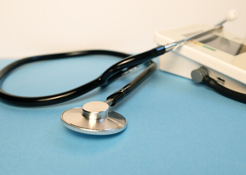 Close-up of a medical stethoscope in sharp focus with a blurred digital blood pressure monitor in the background. Healthcare, cardiology and medical examination concept.