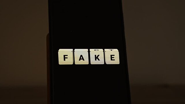 Letter cubes on a smartphone in a dim room spell FAKE, then the last two flip and the word becomes FACT. A sharp visual for fact checking, fighting fake news and disinformation, truth versus lies and