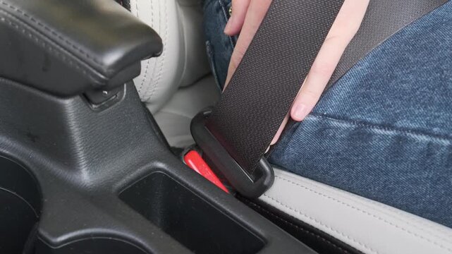 Female driver fastens safety seatbelt buckle securely inside modern car interior before starting road journey, practicing responsible automotive travel precautions with calm focus and care