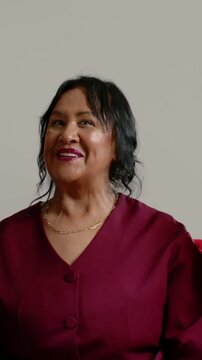 Vertical video: Smiling senior in wine gold chain tucking hair in set as pal entering in red blazer