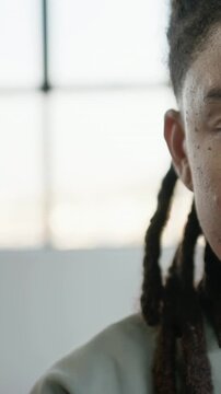 Vertical video: Looking man with dreads turning, showing cheek at grid window, light top