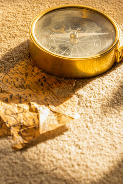 Vintage brass compass and old map partly buried in sand in sunlight background backdrop
