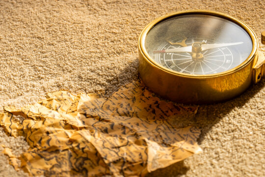 Vintage brass compass and old map partly buried in sand in sunlight background backdrop