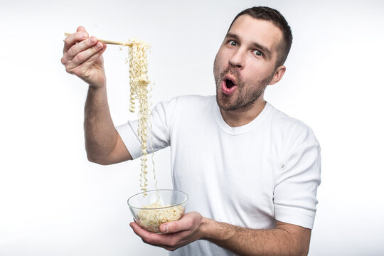A picture of guy that likes to eat oriental cuisine. He has a plate of thai spaghetti and keep it with special sticks for food. Also this weird guy likes to eat junk food. Isolated on white.
