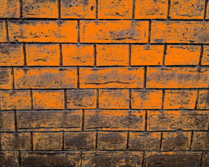 A dramatic close-up background capturing an old brick wall partially coated or stained with a highly saturated, vivid orange color, creating a striking contrast with the dark horizontal mortar joints  © Usman